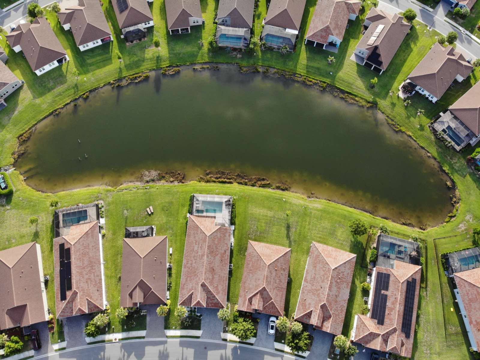 Aerial photo of a crescent-shaped stormwater pond with open water and a mowed grass bank running to the shoreline.